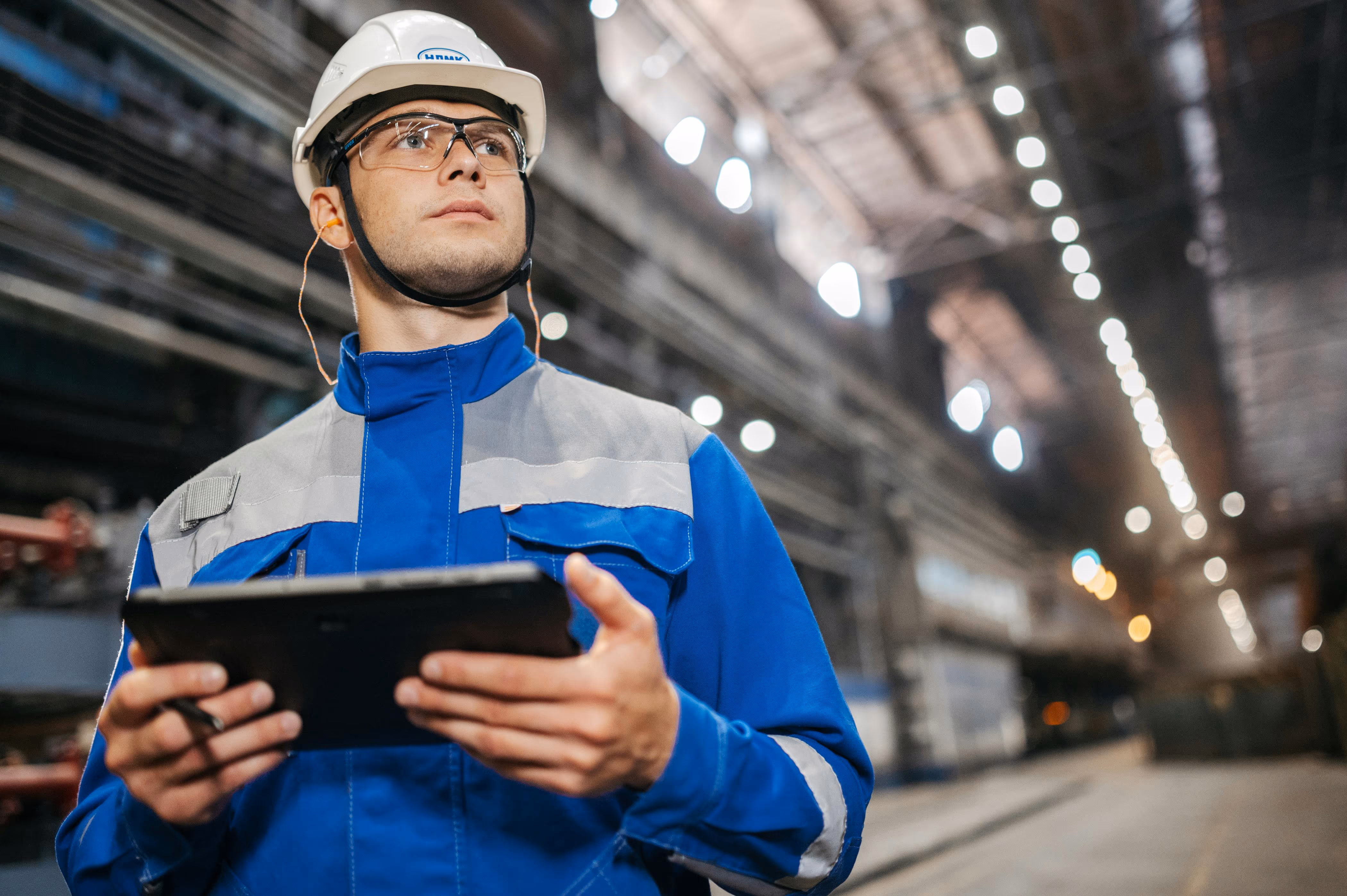 Ispettore tecnico con casco e tablet effettua sopralluogo in capannone industriale